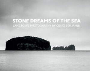 Black and white seascape of two islands silhouetted against the dawn sky, with text "Stone Dreams of the Sea: Landscape Photography by Craig Benjamin"